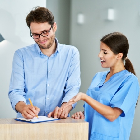 Man writing on clipboard with female dental team member