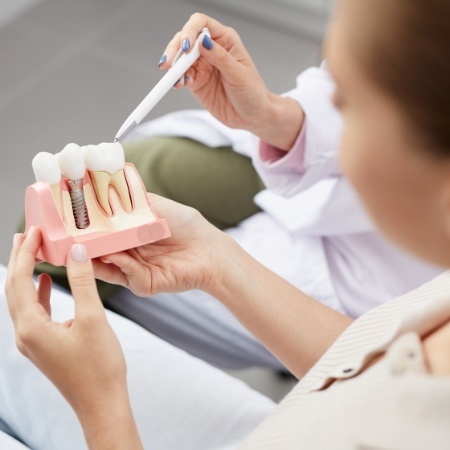 Woman sitting in dental chair holding model of dental implant