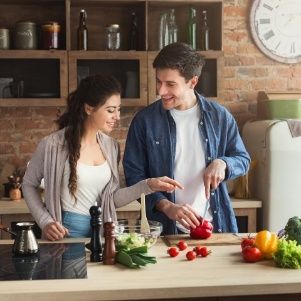 Man and woman in kitchen cutting up vegetables