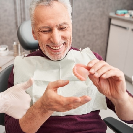 Smiling dental patient holding a full denture