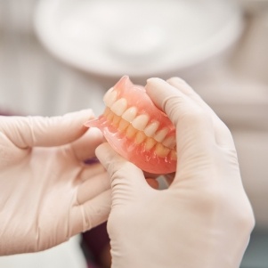 Gloved hands holding two full dentures