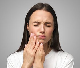 a woman holding her cheek due to tooth pain