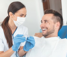 Dental assistant holding clear aligner and smiling at patient