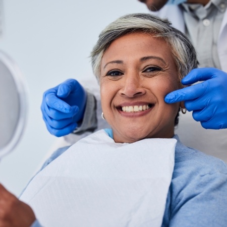 Woman sitting in dental chair with dentist pointing to smile