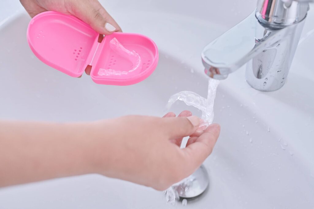 Patient rinsing clear aligner in sink